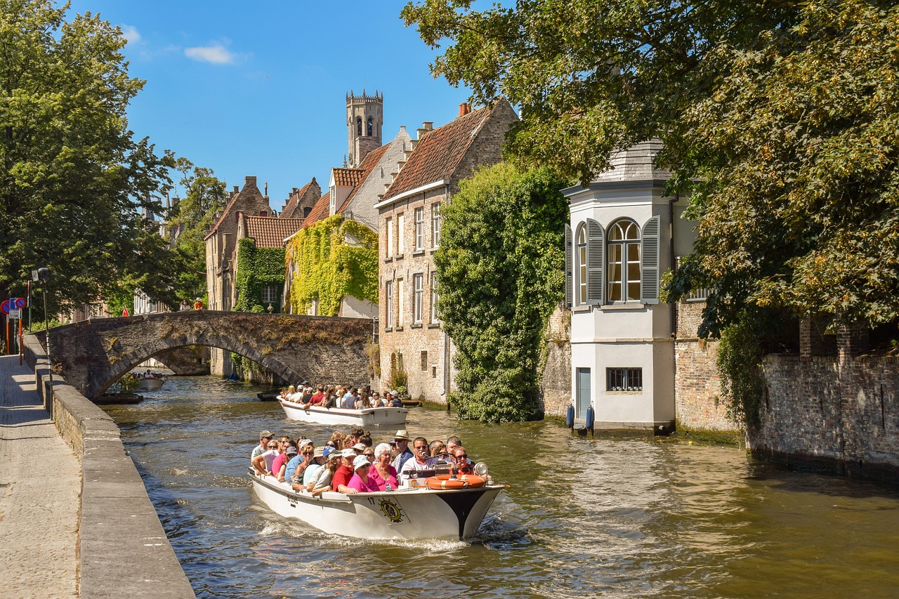 In this image, a group of individuals is depicted seated in vessels. Additionally, a bridge, several poles, a group traversing a path, a building with windows, a wall, and a cloudy sky are visible.\n
