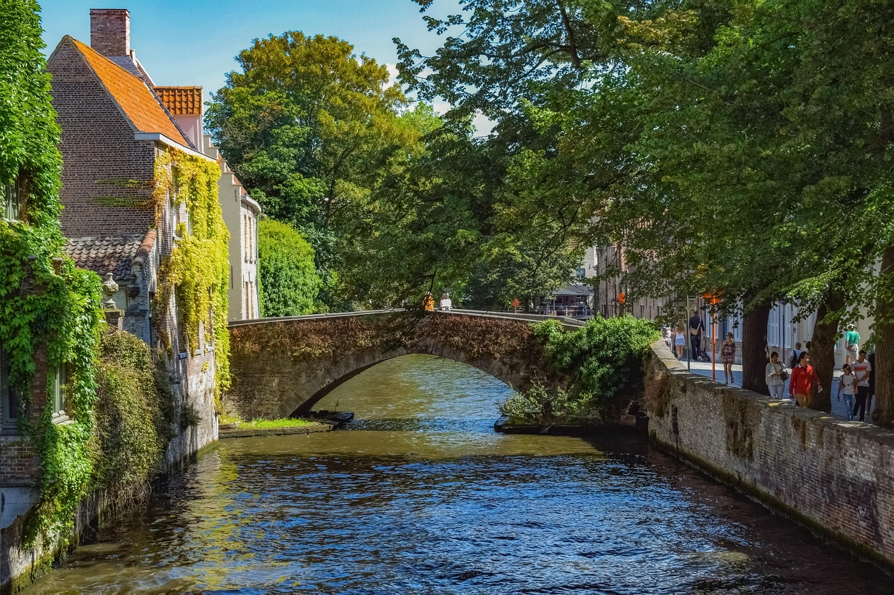 In this image, a bridge, water, buildings, trees, people, the sky, and clouds are depicted in a painting.\n
