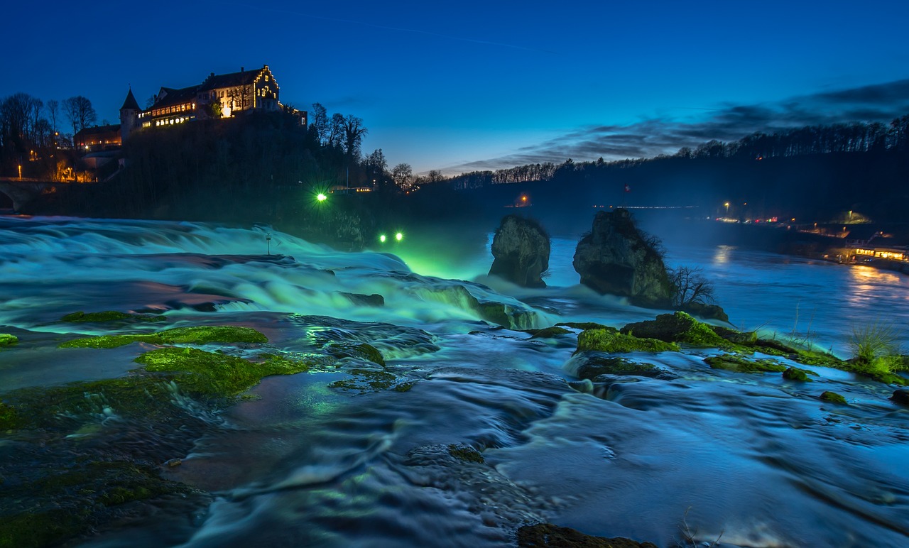 In this photograph, a building, trees, lights, water, and sky are visible.\n
