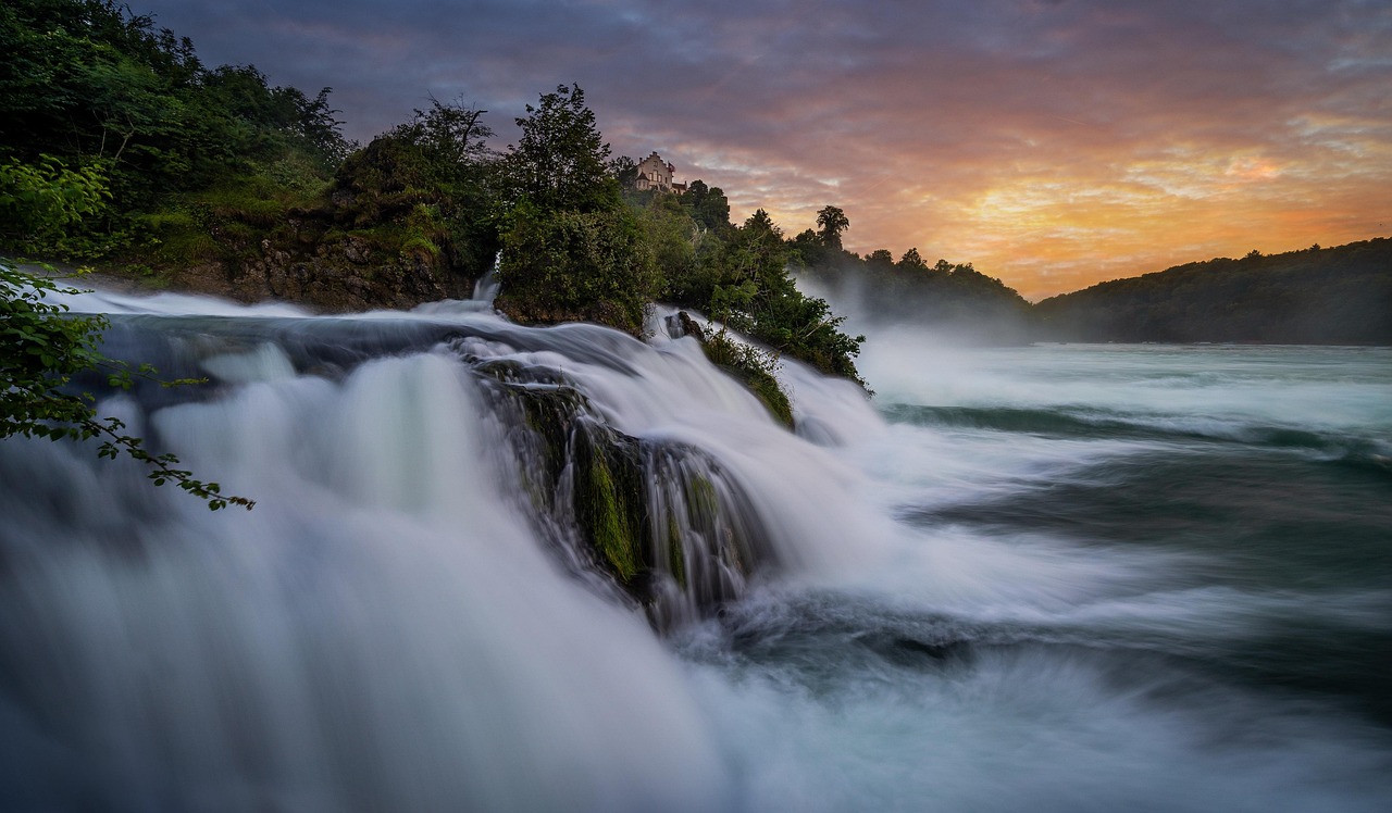 In this image, a waterfall is depicted in the foreground. The background features a collection of trees and a vast expanse of sky.\n
