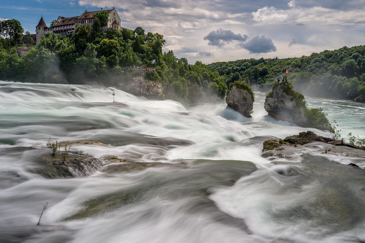 In this image, a building, trees, rocks, water, and sky with clouds are visible.\n
