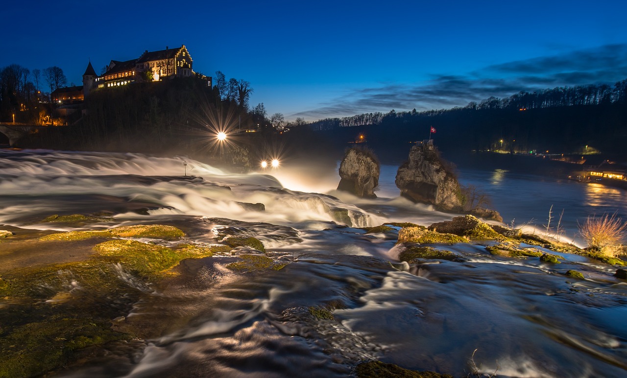 In this photograph, a building, trees, lights, water, and sky are visible.\n
